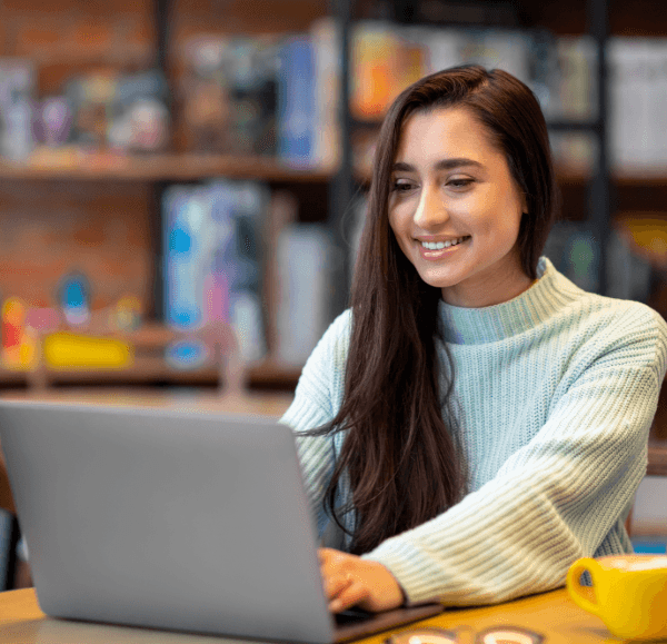 Woman smiling while using a laptop in library.